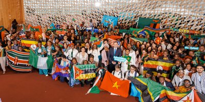 Photo taken from above, looking down at a crowd of people smiling and holding up the flags of several countries form around the world.