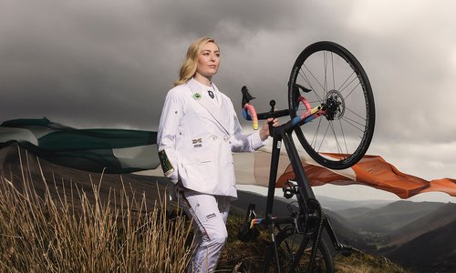 A female athlete dressed in the white Olympic uniform, holding her bike.