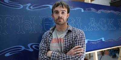 Lockie standing in front of an in progress handpainted sign