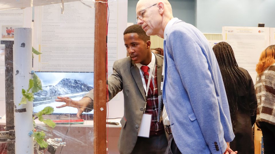 young man in white shirt singing with microphone hanging above him with irish road projected behind him