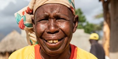 A woman looks at the camera holding a document. The sun is shining in her face.