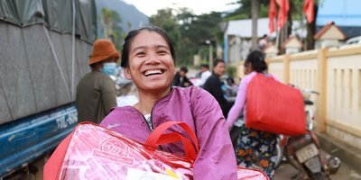 A smiling woman hold a large red plastic bag, which has the Irish Aid logo and the words 'Government of Ireland'.