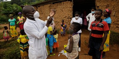 A doctor wearing a white mask and coat administers an injection to children.
