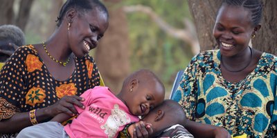 Two mothers watching their two children cuddle.