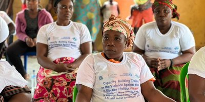 Women sit wearing white t-shirts with the text 'Capacity building training on the violence against women in election / politics'