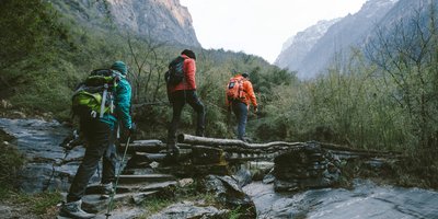 Three people in walking gear crossing a bridge in the valley between two mountains