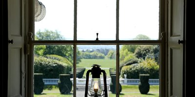 oil lamp in a window looking out on a large lawn and gardens