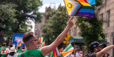 A man in a green tshirt with a rainbow on the back raising the Progress Pride Flag during the New York City Pride March