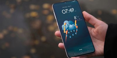 A hand holding a phone with a storm weather warning, there are raindrops on the phone screen