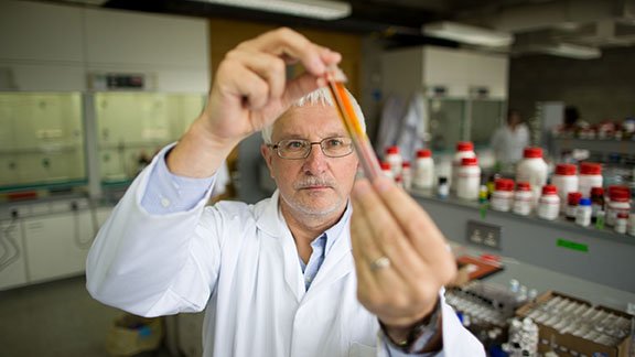 man in a white coat in a lab holding up a vial