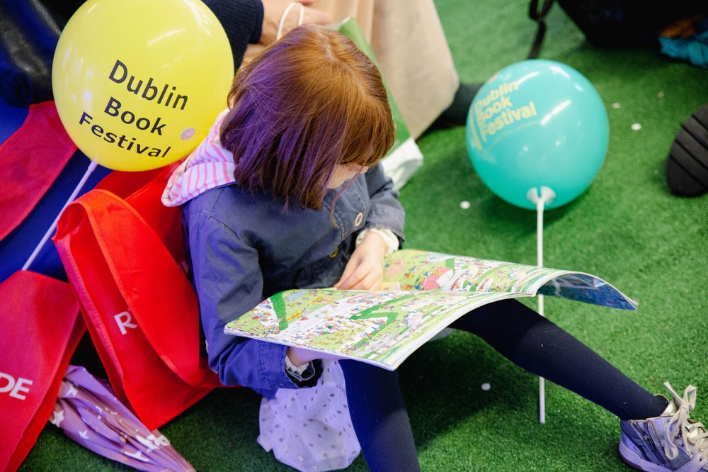 Child reading a book sitting on the floor surrounded by balloons at Dublin Book Festival