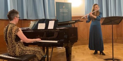 Elaine Loebenstein playing piano as a flautist accompanies her