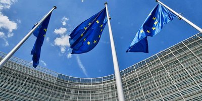 Three blue flags with yellow stars in front of a large office building