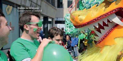 A man dressed in green wearing shamrock shaped glasses watching a float in the St Patrick's Day parade.