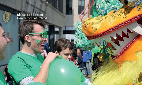A man dressed in green wearing shamrock shaped glasses watching a float in the St Patrick's Day parade.