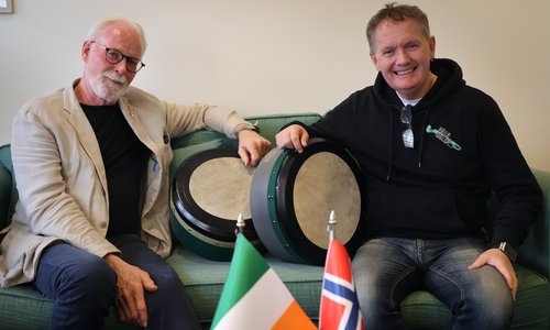 Bjarne Stensrud and Brendan Monaghan sitting with bodhráns in front of an Irish and Norwegian flag
