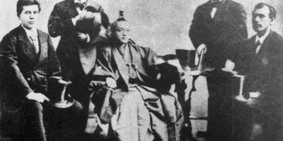 Group of 5 men sitting on chairs in suits