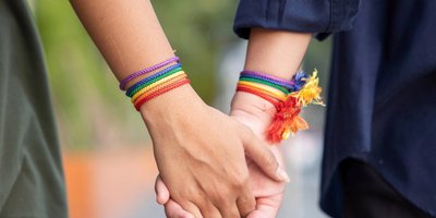 Two people holding hands, both are wearing rainbow bracelets