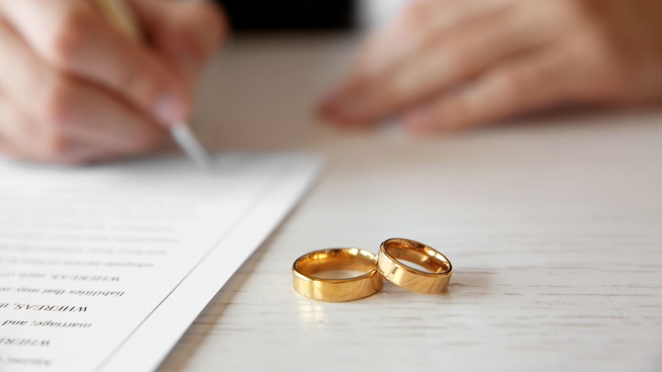 Someone signing a document with wedding rings in the foreground.