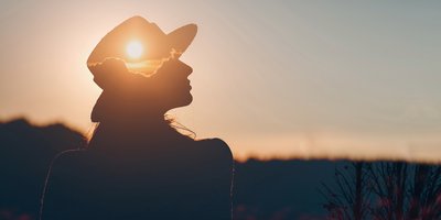 Silhouette of a woman in a hat with a reflection of the sun and clouds on her head