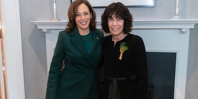 two women in suits standing in front of a fireplace