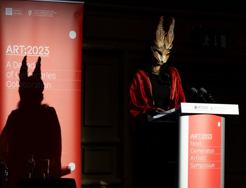 Nidhi Zak on stage doing a reading wearing a cat mask