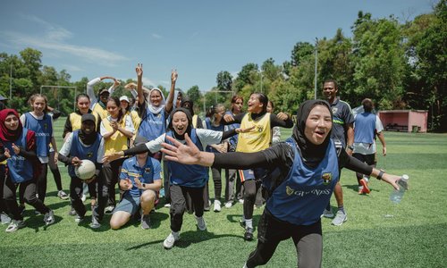 A group of teenagers from different ethnic backgrounds in yellow and blue sports bibs, running happily toward the camera