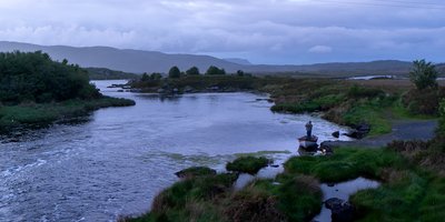 A gloomy view of a lake where a lone man is setting out on his small fishing boat.