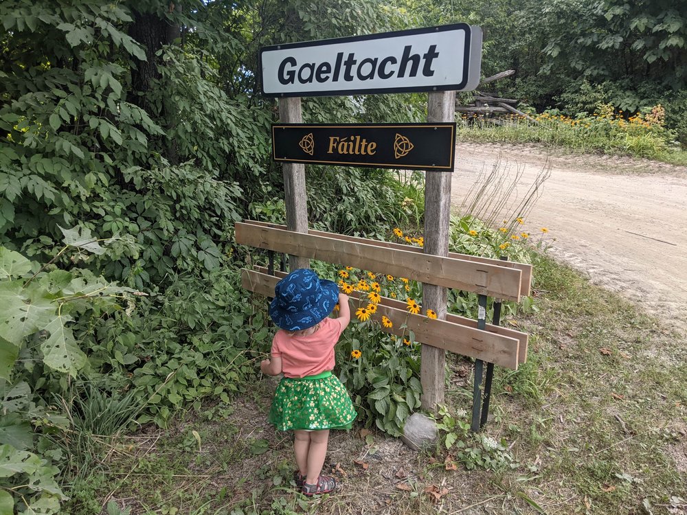 A young girl pointing to signs reading 'Gaeltacht' and 'Failte'