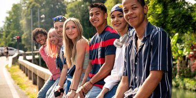 A group of seven teenagers of different genders and ethnicities sat on a fence outdoors