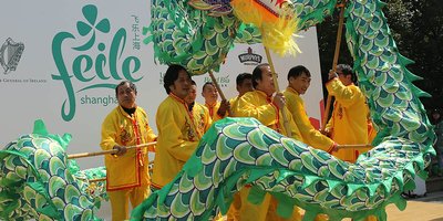 A green Asian parade dragon being carried by eight men in orange suits.