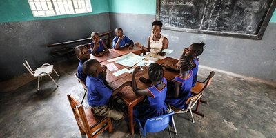 A teacher sits with a group of young pupils at a large table.