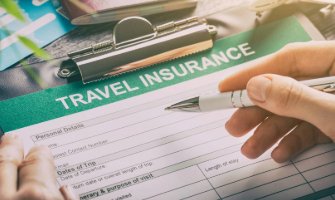 Someone holding a pen over a form on a clipboard titled 'Travel Insurance', there are passports and boarding passes in the background