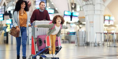 Mother and father pushing their daughter on a luggage trolley with suitcases. The little girl is pretending to fly.