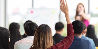 Someone in a classroom setting with their hands raised