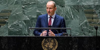 one man in blue suit speaking at a podium with a crest on it