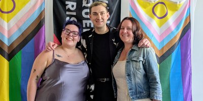 three people standing front of pride flags