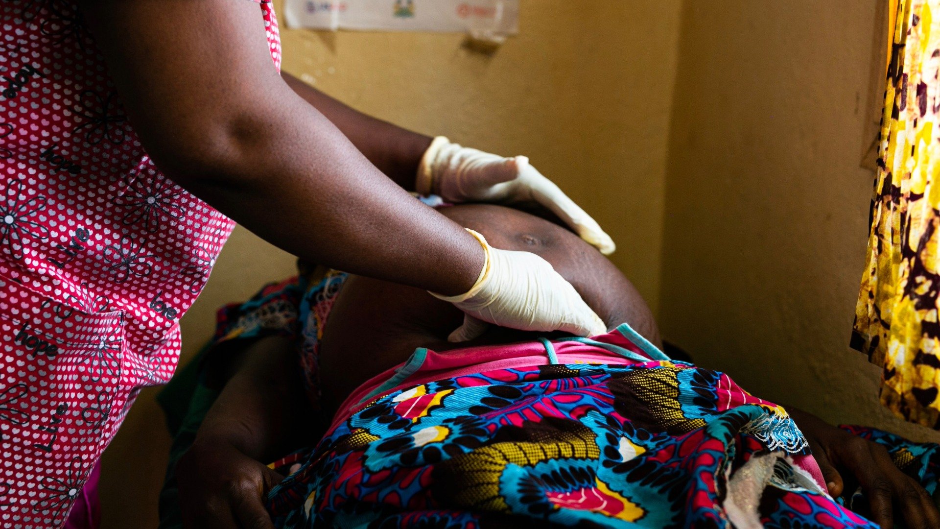 Medical practitioner wearing gloves performing an examination on a pregnant person by touching her belly