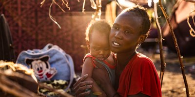 A woman holds a baby in her arms as the setting sun shines on them.