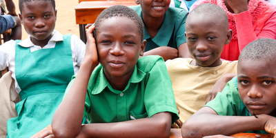 Schoolchildren sit at desks and look at the camera.