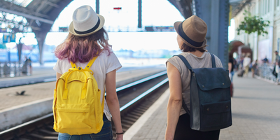 Two female students wearing backpacks at a train station